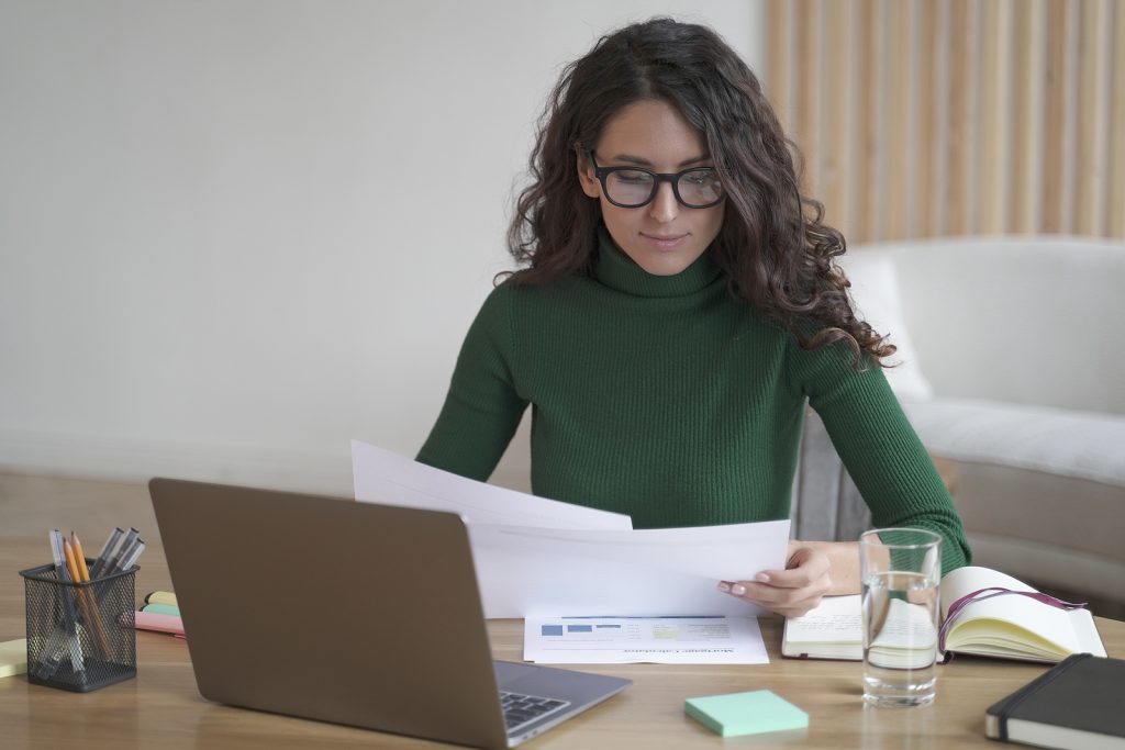 Young Focused Spanish Woman Freelancer In Glasses Analyzing Docu