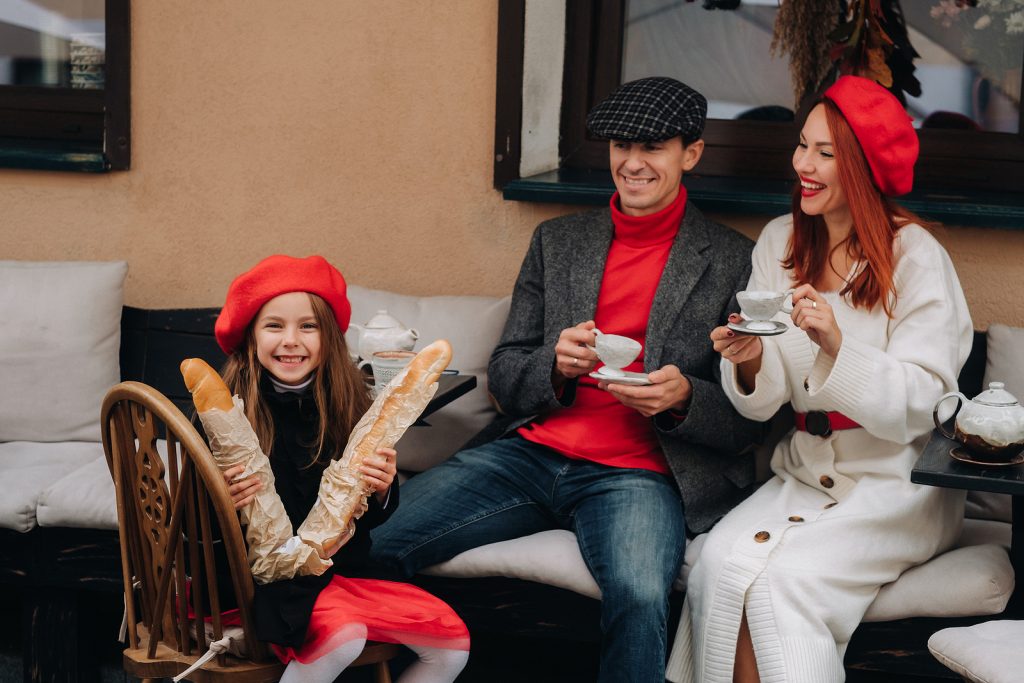 A Stylish Family Of Three Is Sitting At A Table Outside In A Caf