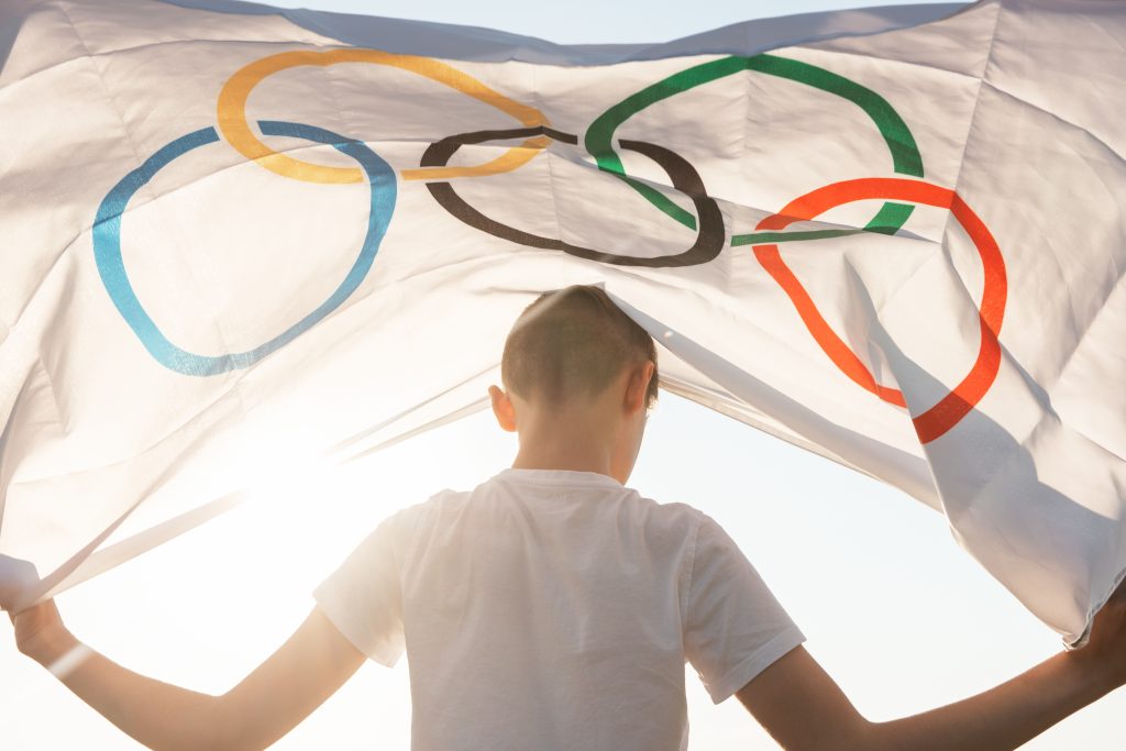 Portrait of boy waving flag the Olympic Games outdoors over clou
